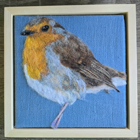 Felted robin on a blue linen background with a wooden frame