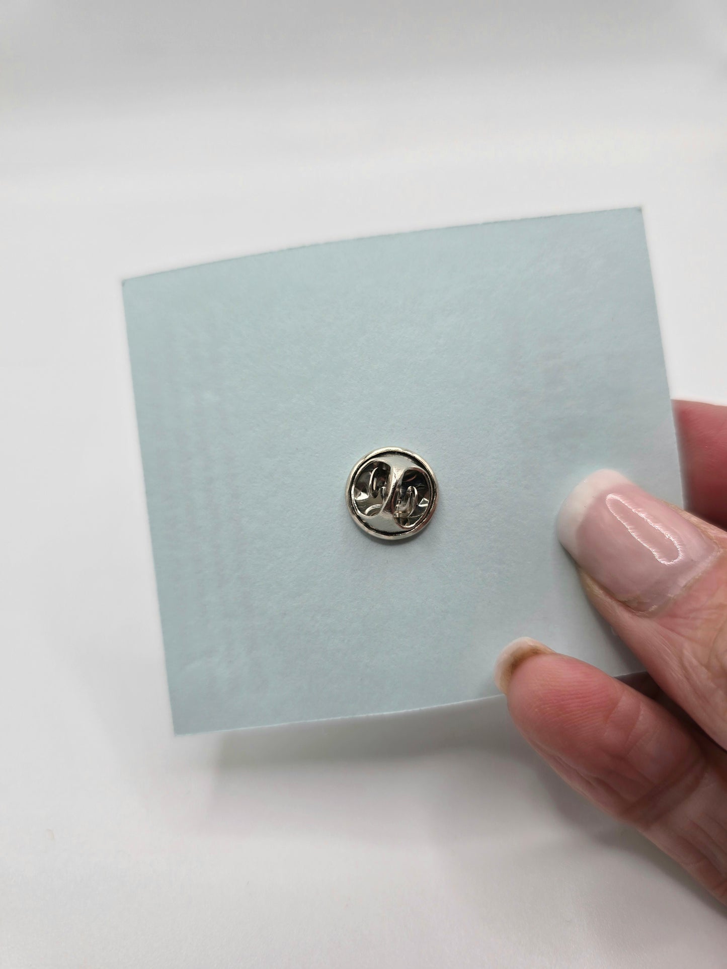 Small round metal pin on a light blue card held by a hand against a white background