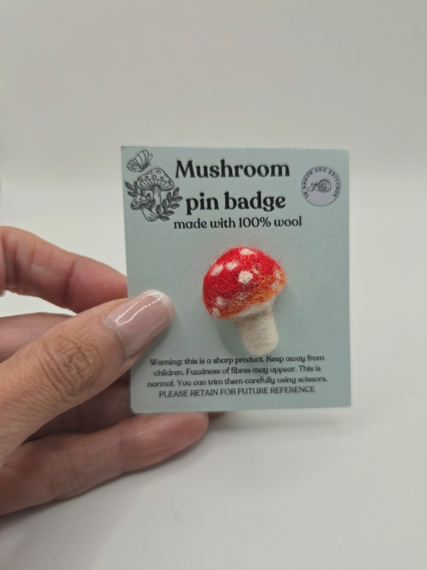 Mushroom pin badge on a card held by a hand against a white background