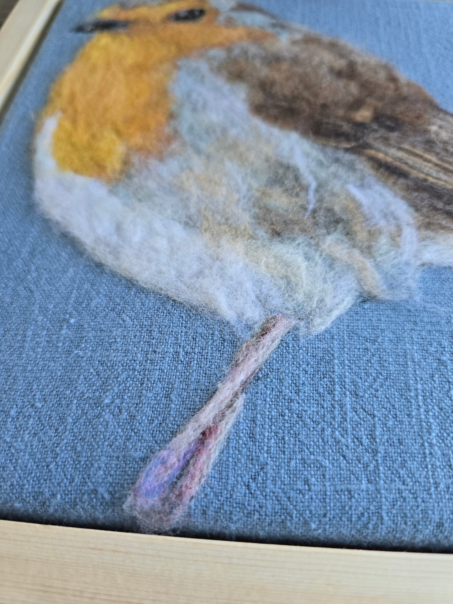 Close-up of a needle felted piece on fabric with a detailed depiction of a robin.