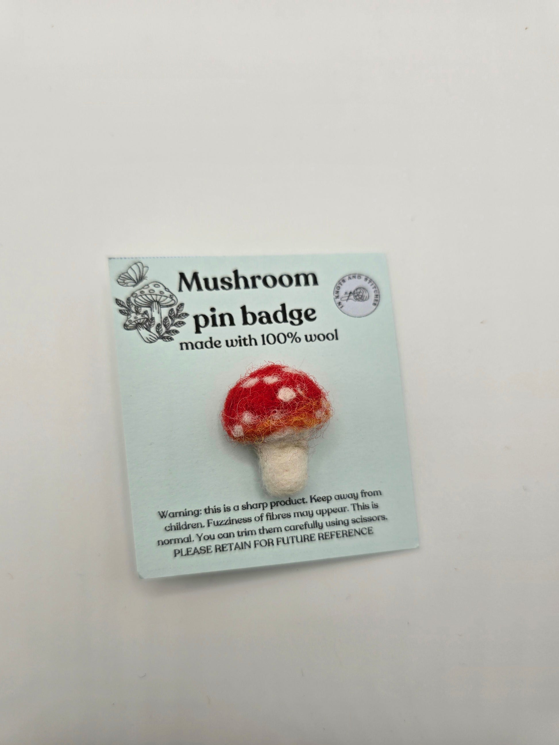 Mushroom pin badge on a card with text about material and care instructions.