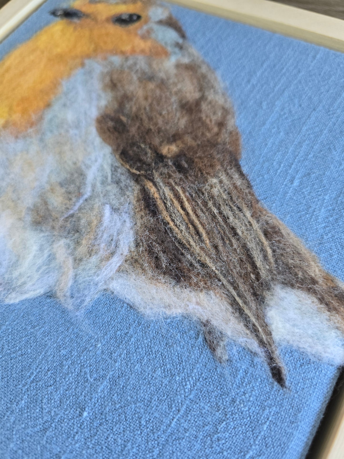 Close-up of a needle felted robin on a textured blue fabric background