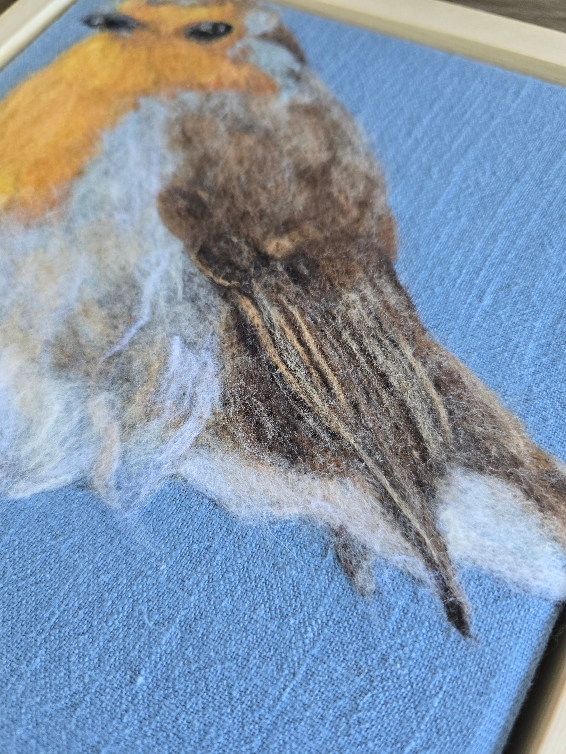 Close-up of a needle felted robin on a textured blue fabric background