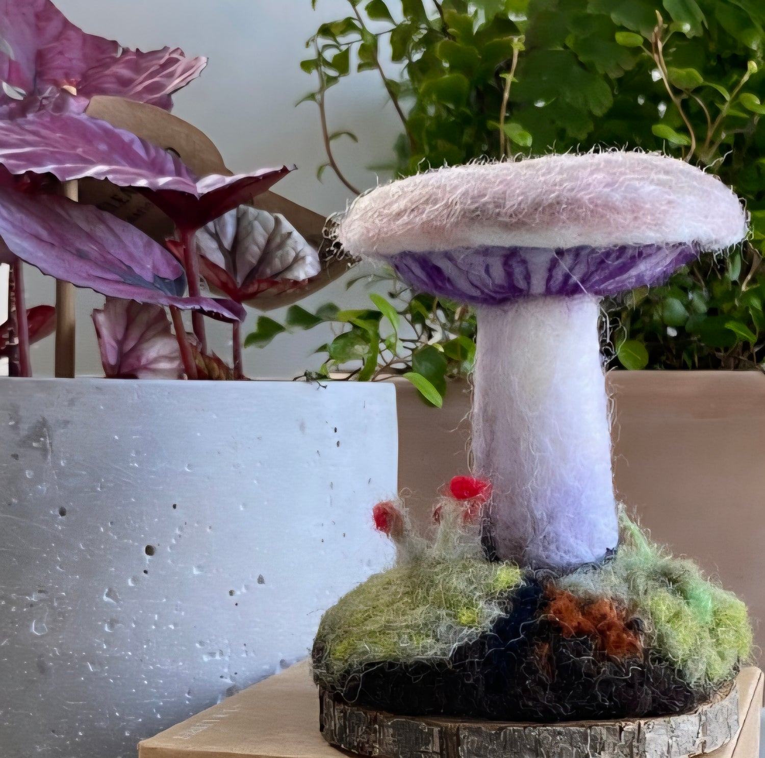 Felted mushroom decoration on a wooden base with plants in the background